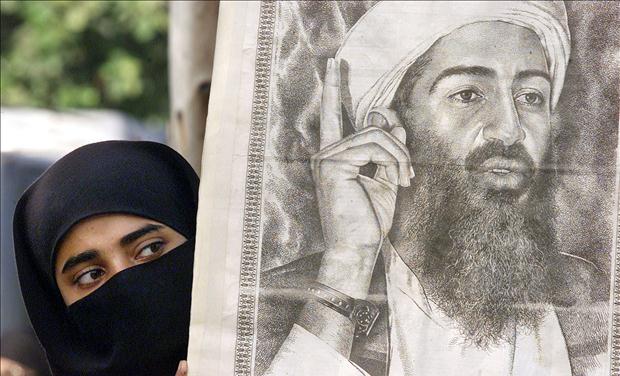 A PAKISTANI WOMAN PEERS AROUND A POSTER OF OSAMA BIN LADEN IN KARACHI.