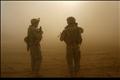 A U.S. soldier stand walk in a cloud of dust as a Blackhawk helicopter takes off during a mission in southern Baghdad