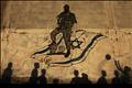 The shadows of Palestinian children are cast against a wall as they play with a ball in front of an anti-Israel mural in Gaza City
