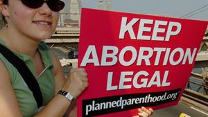Planned Parenthood abortion rights protester signals Brooklyn Bridge traffic.